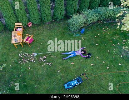 Image aérienne d'une jeune fille allongé sur une pelouse fraîchement coupée avec son chien, en appréciant l'herbe verte après la tonte.Tirer à partir d'un drone Banque D'Images