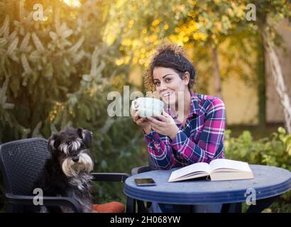 Fille et chien assis sur des chaises dans le parc.Boire du thé et faire une pause pour étudier Banque D'Images