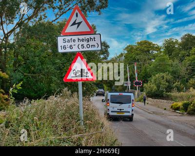 Les véhicules passent des panneaux d'avertissement indiquant que les câbles électriques aériens sont en hauteur et qu'ils présentent un risque de mise à la terre lorsqu'ils approchent d'un passage à niveau à Beal, dans le Northumberland, au Royaume-Uni. Banque D'Images
