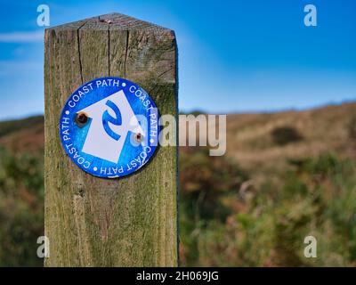 Un panneau circulaire, bleu et blanc fixé à un poteau en bois abîmé pointe vers le chemin de la côte de Northumberland, dans le nord-est de l'Angleterre, au Royaume-Uni Banque D'Images