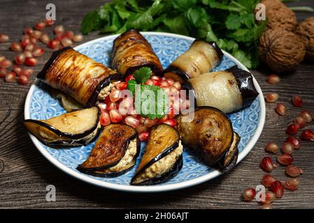 Rouleaux d'aubergines et de poivrons avec farce de noix sur une assiette bleue avec graines de grenade.Cuisine géorgienne.8 portions, garnies de feuilles de coriandre. Banque D'Images