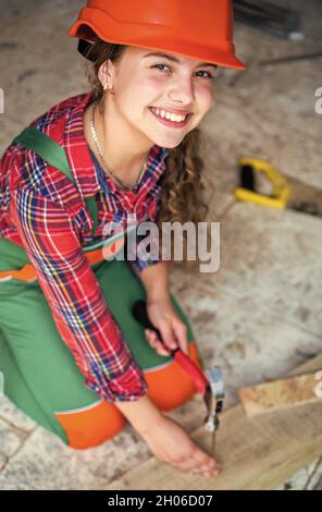 Portrait d'un enfant mignon posant comme un menuisier, avec un marteau. Travaillant comme menuisier. charpentier dans le travail de chapeau de protection. Fille travaillant avec le bois dans Banque D'Images