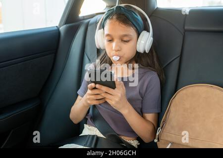 Adorable écolière avec gommage à bulles dans un smartphone tout en écoutant de la musique dans un casque Banque D'Images