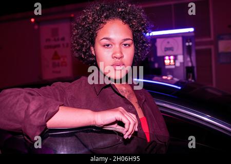 Jolie femme vous regardant en sortant de la voiture électrique à la station-service Banque D'Images