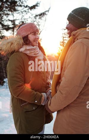 Les jeunes souriants sont des vêtements d'hiver qui se regardent les uns les autres tout en se tenant à la main dans le parc hivernal Banque D'Images