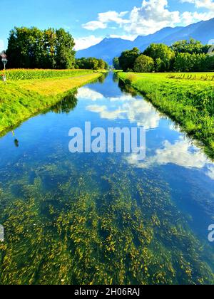 Rivière qui coule à travers les champs verts dans la campagne avec le ciel bleu se reflétant dans l'eau Banque D'Images