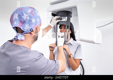 Dentiste de sexe masculin ajustant une machine de blanchiment des dents utilisée par une patiente dans une clinique dentaire Banque D'Images