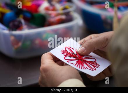 Gros plan des mains d'une femme adulte triant la forme d'une fleur sur du papier avec de la laine Banque D'Images