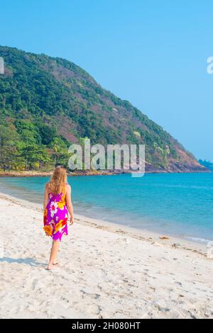 Une femme aux longs cheveux blonds marche le long de la plage de sable parmi les palmiers sur une île tropicale en Thaïlande. Banque D'Images