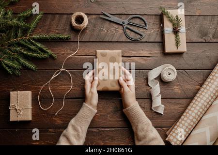 Vue de dessus arrière-plan de Noël avec femme méconnaissable empaquetage de cadeaux à table en bois, espace de copie Banque D'Images