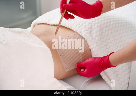 Jeune femme obtenant un traitement de corps de levage de peau réductif de graisse par un cosmétologue.Belle patiente qui apprécie les contours du corps amincissants Banque D'Images