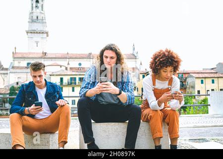 Groupe multiculturel d'amis utilisant des téléphones mobiles - étudiants assis dans une rangée et tapant sur un smartphone Banque D'Images