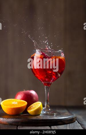 Sangria en verre avec des éclaboussures et des ingrédients - orange, citron et pomme, fond en bois sombre Banque D'Images