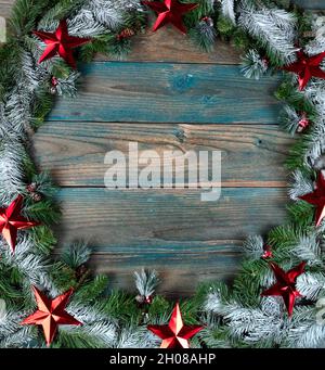 Vue en hauteur d'une couronne couverte de neige avec des étoiles brillantes rouges dans la bordure circulaire sur des planches de bois vieillies bleues pour les vacances d'hiver de Noël ou Banque D'Images