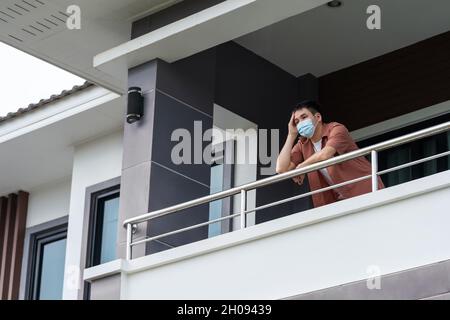 homme portant un masque facial et la quarantaine dans le balcon de sa maison, coronavirus (covid-19) concept pandémique Banque D'Images