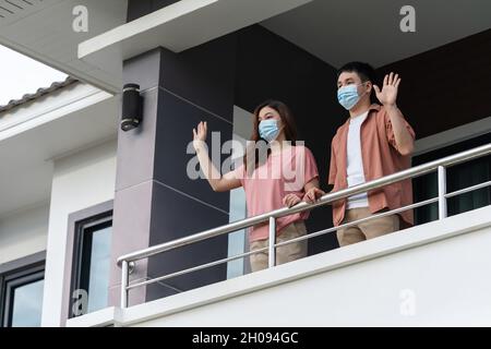 quarantaine couple portant un masque facial et salutation voisins du balcon de la maison, coronavirus(covid-19) pandémie Banque D'Images