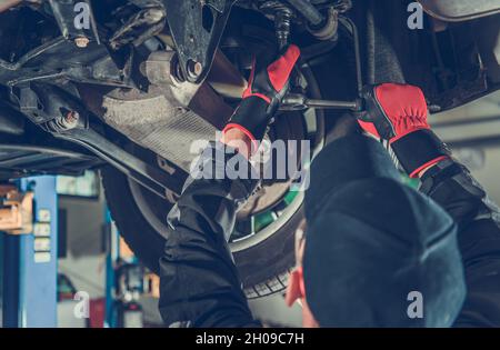 Automobile Caucasien mécanicien travaillant sous un véhicule.Tâche de maintenance de la suspension.Service de voiture régulier. Banque D'Images