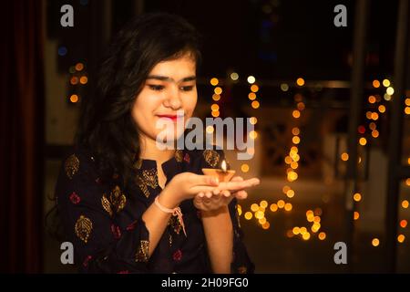 Bonne jeune indienne souriante belle femme tenant diya / argile lampes à l'huile portant des vêtements traditionnels, célébrant diwali, intérieur.magnifique femme dans l'ethnie d Banque D'Images