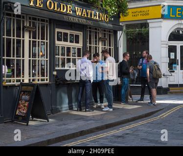 Deux groupes de jeunes hommes apprécient un verre à l'extérieur du pub Ye Olde Watling à Watling Street, City of London, Angleterre, Royaume-Uni Banque D'Images