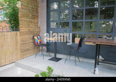 Table et chaise vides devant un petit café.Un oreiller coloré sur une chaise. Écrans en osier et vitrine de menuiserie en fer. Banque D'Images