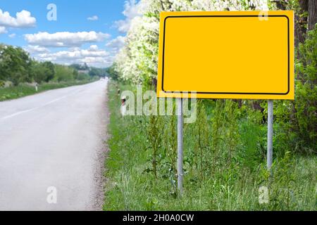 Panneau jaune vierge le long de la route pour le nom du lieu lors d'une belle journée de printemps.Vider l'affiche jaune, l'avertissement et l'avertissement.Tableau d'affichage vierge jaune. Banque D'Images