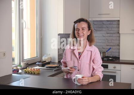 Portrait de femme authentique avec macaron et tasse de thé dans les mains sur son confortable kinchen à la maison. Banque D'Images