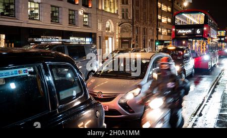 La circulation nocturne s'est bloquée dans les rues humides de Londres's Strand.Flou de mouvement d'un scooter passant le trafic stationnaire. Banque D'Images