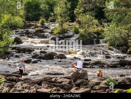 Visiteurs assis sur des rochers aux chutes de Dochart, sur la rivière Dochart, juste à l'extérieur du village de Killin, Stirlingshire, Écosse Banque D'Images