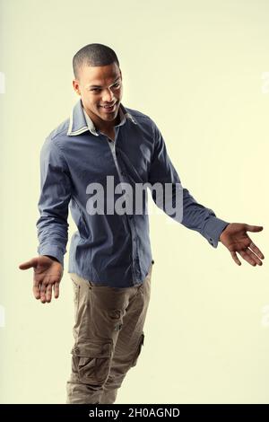 Charismatique jeune Noir homme gestant avec ses mains comme il donne à la caméra un sourire aimable dans un trois quarts de portrait sur jaune Banque D'Images