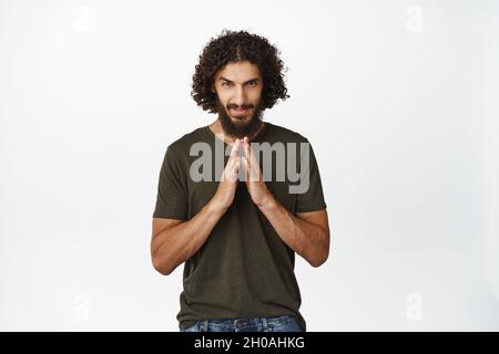 Un homme du Moyen-Orient cupide et détestant un plan, vole les doigts comme le génie du mal, l'idée à l'esprit, se tenant sur fond blanc Banque D'Images