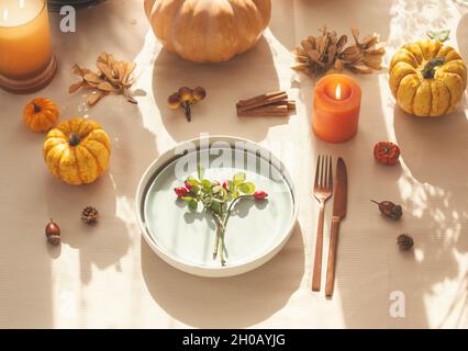 Table d'automne avec citrouilles, bougies en feu, glands et assiette avec hanche rose et couverts sur la table avec nappe beige.Confortable, ensoleillé conc. D'automne Banque D'Images