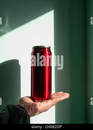 Bouteille Thermo-bidon rouge dans les mains mâles bleu turquoise mur fond ombre dure.Thé chaud café boissons boire en automne froid hiver temps.Dura Banque D'Images