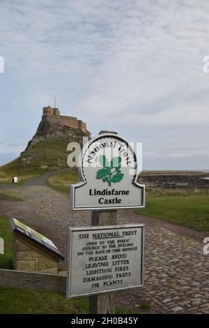 Panneau pour le château de Lindisfarne avec fond flou de chemin, château et ciel bleu avec des nuages.Faible profondeur de champ. Banque D'Images