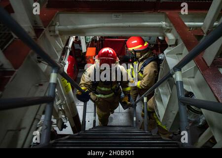 210116-N-NC885-1105 MER D'OMAN DU NORD (JANV16, 2021) le technicien des systèmes d'information de 2e classe Jakob Aganon, de Las Vegas, (à gauche) et le spécialiste des services de détail de 3e classe Juan Bueno Barrios, de Pembroke Pines, FLA, montent une échelle bien après avoir trouvé et éteint un feu simulé pendant un forage de quartier général à bord du destroyer de missile guidé USS Sterett(DDG 104).Sterett fait partie du Nimitz Carrier Strike Group et est déployé dans la zone d'opérations de la 5e flotte des États-Unis pour assurer la stabilité et la sécurité maritimes dans la région centrale, reliant la Méditerranée et le Pacifique à travers Banque D'Images