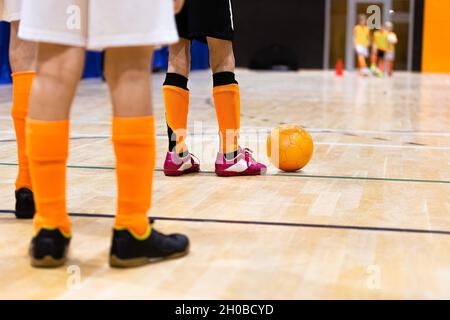 Enfants sur l'entraînement de football en salle.Enfants jouant à Futsal sur un sol en bois.Jambes des enfants joueurs de football avec le ballon Futsal d'Orange.Joueurs debout en deux Banque D'Images