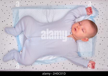 Le bébé dort dans une posture en forme d'étoile avec ses bras et ses jambes écartées sur un lit d'enfant.Enfant de trois mois Banque D'Images
