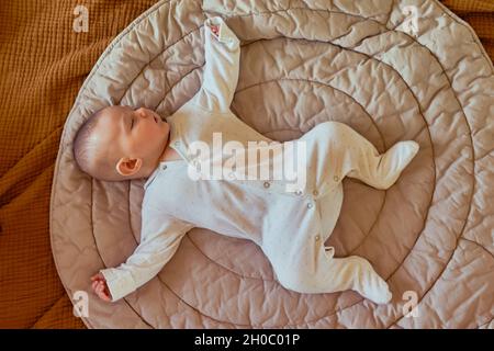 Le bébé dort dans la grenouille poser sur le tapis, vue de dessus.L'enfant dort avec ses bras et ses jambes étalées sur les côtés Banque D'Images