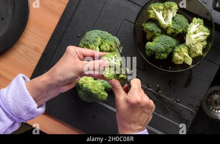 Préparer et trancher des brocolis verts (Brassica oleracea) à la main pour le déjeuner dans la cuisine, vue d'en haut Banque D'Images