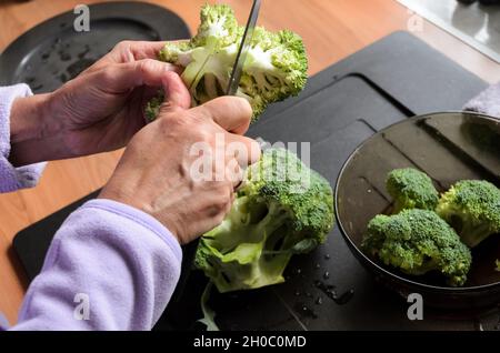 Préparer et trancher des brocolis verts (Brassica oleracea) à la main pour le déjeuner dans la cuisine, vue d'en haut Banque D'Images