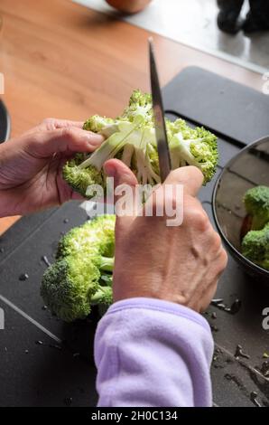 Préparer et trancher des brocolis verts (Brassica oleracea) à la main pour le déjeuner dans la cuisine, vue d'en haut Banque D'Images