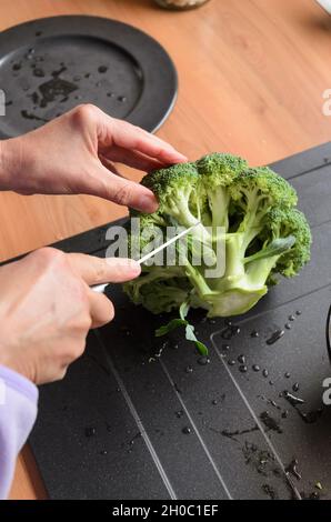 Préparer et trancher des brocolis verts (Brassica oleracea) à la main pour le déjeuner dans la cuisine, vue d'en haut Banque D'Images