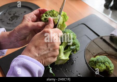 Préparer et trancher des brocolis verts (Brassica oleracea) à la main pour le déjeuner dans la cuisine, vue d'en haut Banque D'Images