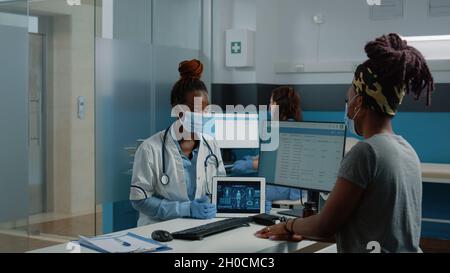 Médecin tenant un comprimé avec analyse du corps humain pour une visite de contrôle avec le patient, portant des masques contre l'épidémie de covid 19.Illustration du squelette pour le soin de l'ostéopathie. Banque D'Images