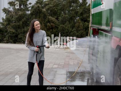 Jolie jeune femme laveur camion avec jet d'eau sous pression au lavage de voiture Banque D'Images