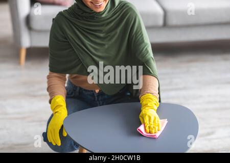 Gros plan d'une jeune femme musulmane qui nettoie la table avec un chiffon Banque D'Images