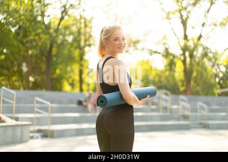Femme sportive Slim vêtements de sport Leggings noirs et escalier en béton tenant le tapis de yoga reposant entre les exercices. Sport et fitness Banque D'Images