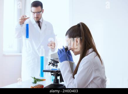 Deux scientifiques font des tests sur les légumes au microscope en laboratoire Banque D'Images