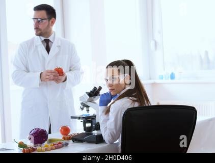 Deux scientifiques font des tests sur les légumes au microscope en laboratoire Banque D'Images