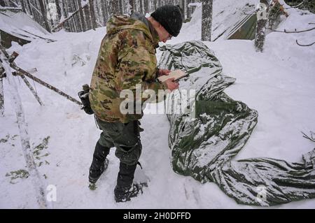 U.S. Air Force Airman Basic Treble Hook, un étudiant dans le cours de formation de spécialiste de survie, d'évasion, de résistance et d'évasion (SERE), renvoie à ses notes lors de l'assemblage de la structure de son abri près de Colville, Washington, le 01 février 2021.Les élèves doivent respecter les délais prévus et utiliser certains nœuds lors de l'assemblage de leurs abris dans lesquels ils dormiront pendant les prochains jours. Banque D'Images