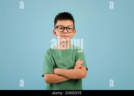 Portrait d'un petit garçon asiatique souriant portant des lunettes debout avec les bras pliés Banque D'Images